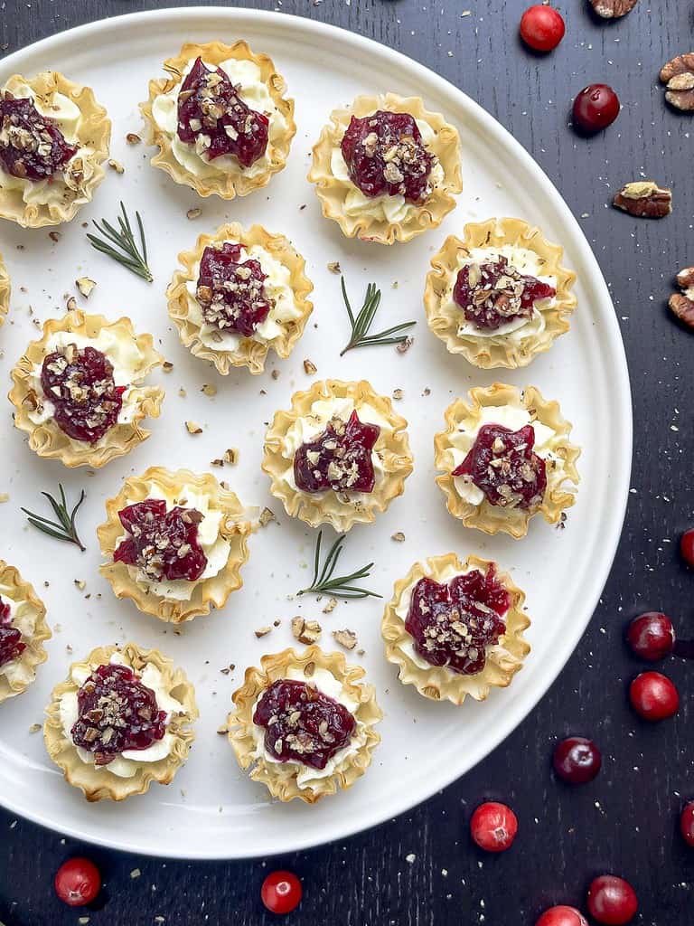 Cranberry tartlets on a round white plate with rosemary and cranberries on the side.
