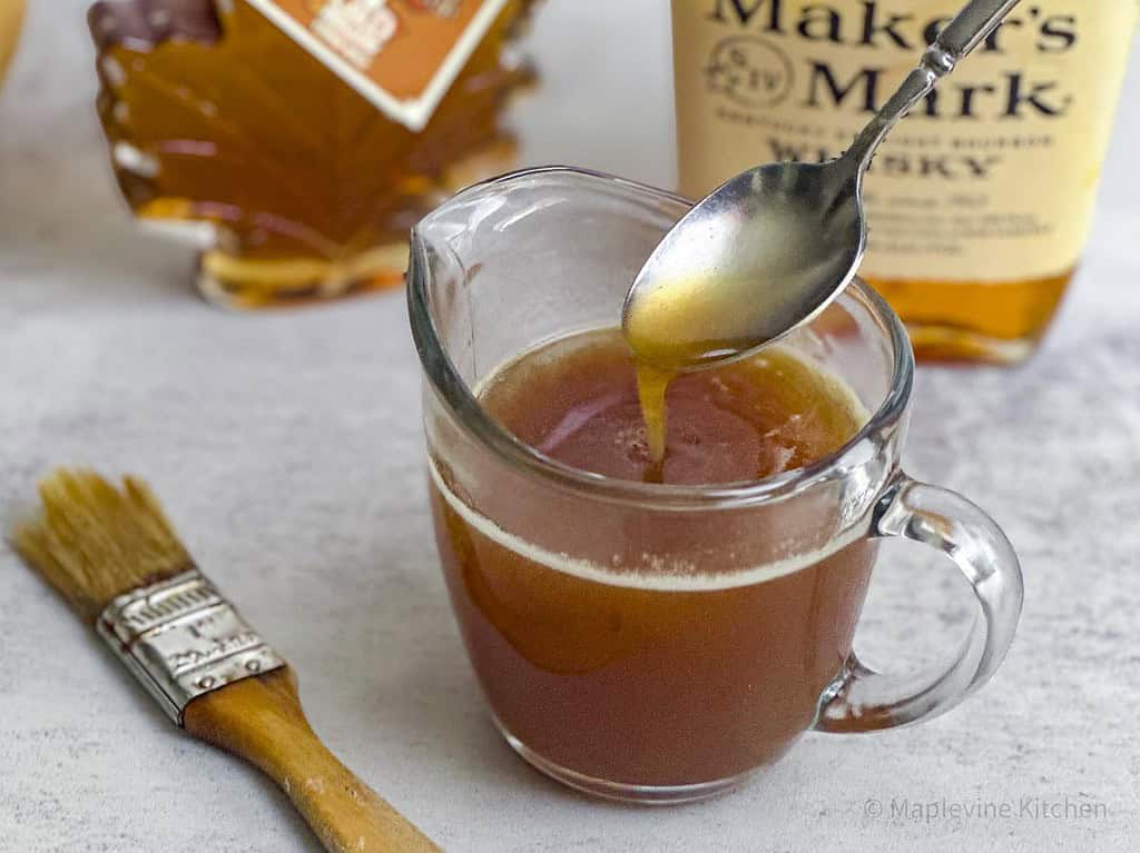 Maple bourbon glaze in a glass cup with a spout with a spoon.