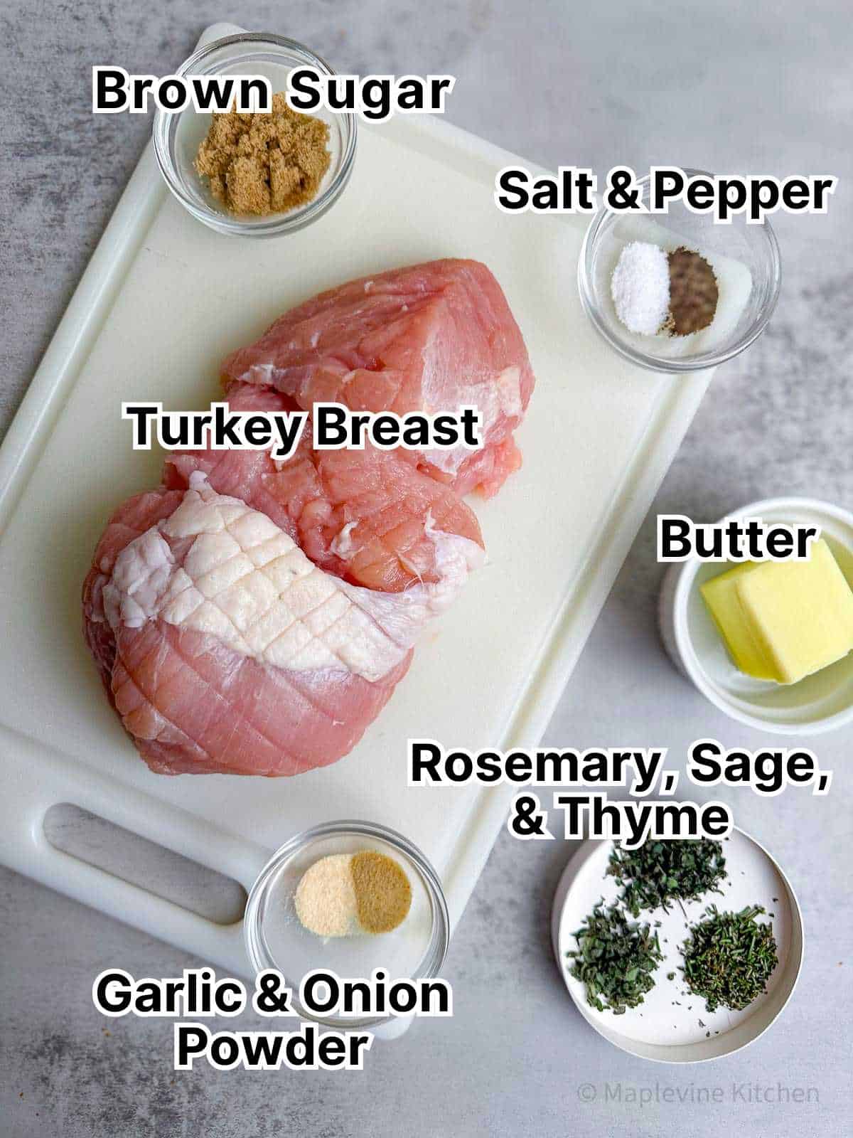 Turkey breast, butter, herbs, and spices on a white cutting board and gray background.
