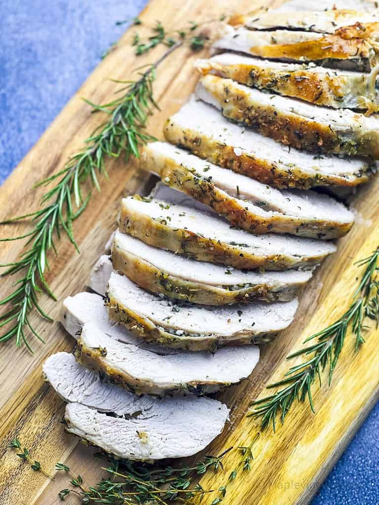 Sliced roasted turkey breast on a wooden board with fresh herbs.