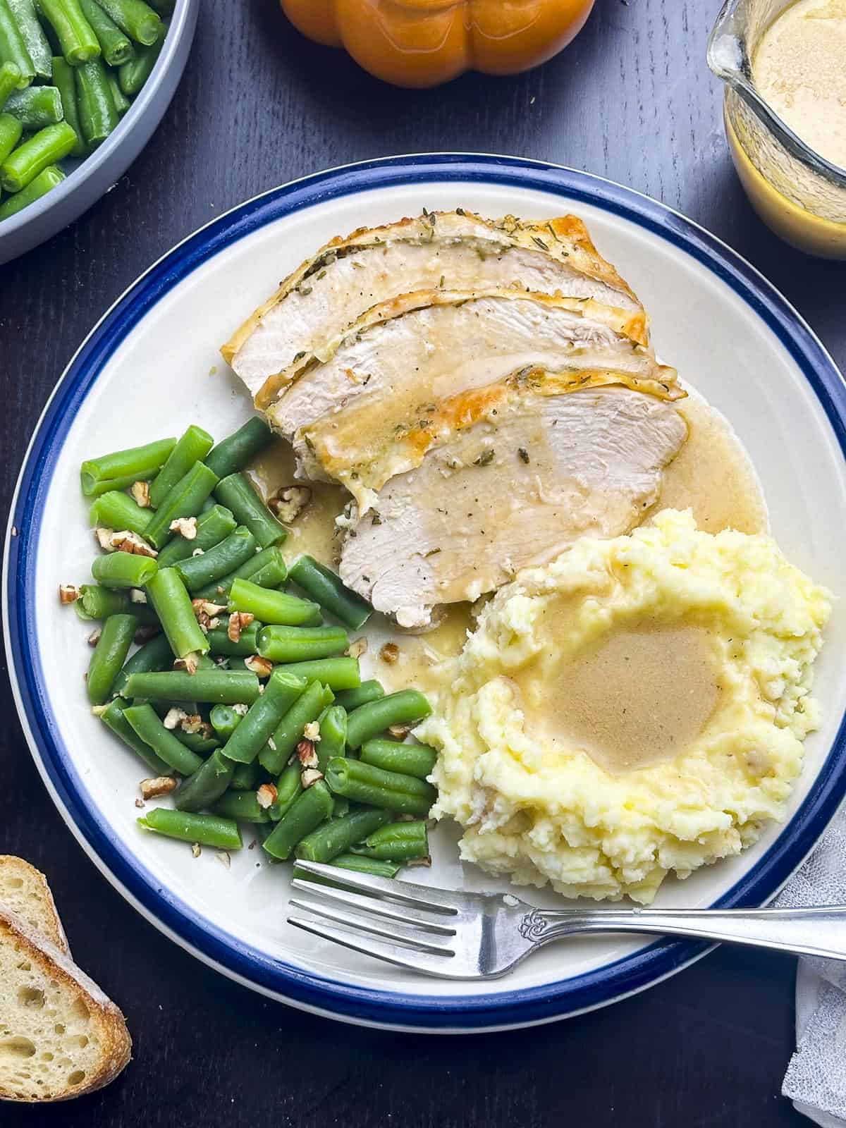 Slices of roasted turkey breast on a plate with mashed potatoes, gravy, and green beans.
