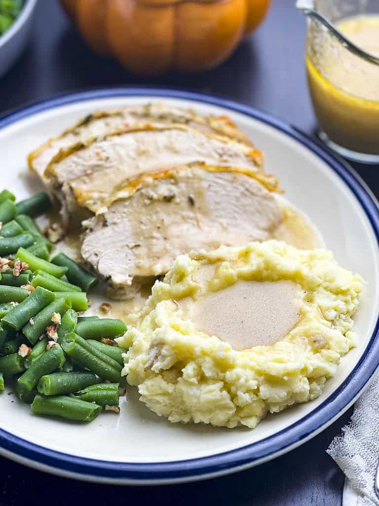 Roasted turkey breast slices on a plate with mashed potatoes, gravy, and green beans.