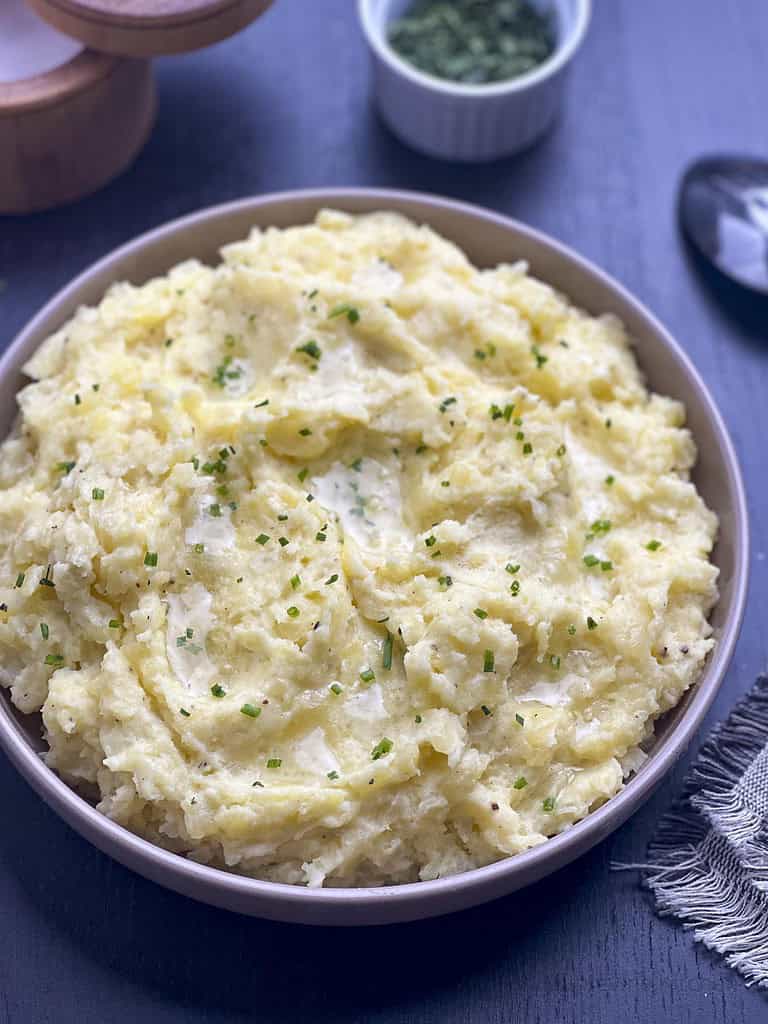 Truffle mashed potatoes in a beige bowl on a dark background.