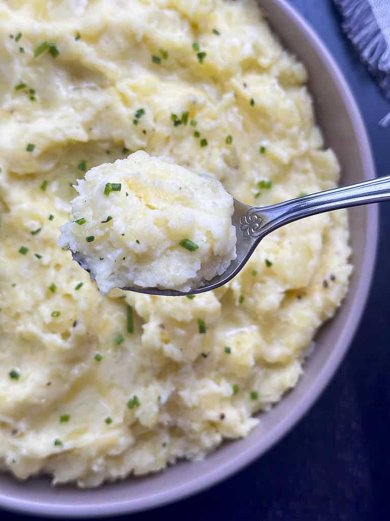 Truffle mashed potatoes in a beige bowl with potatoes on a spoon.