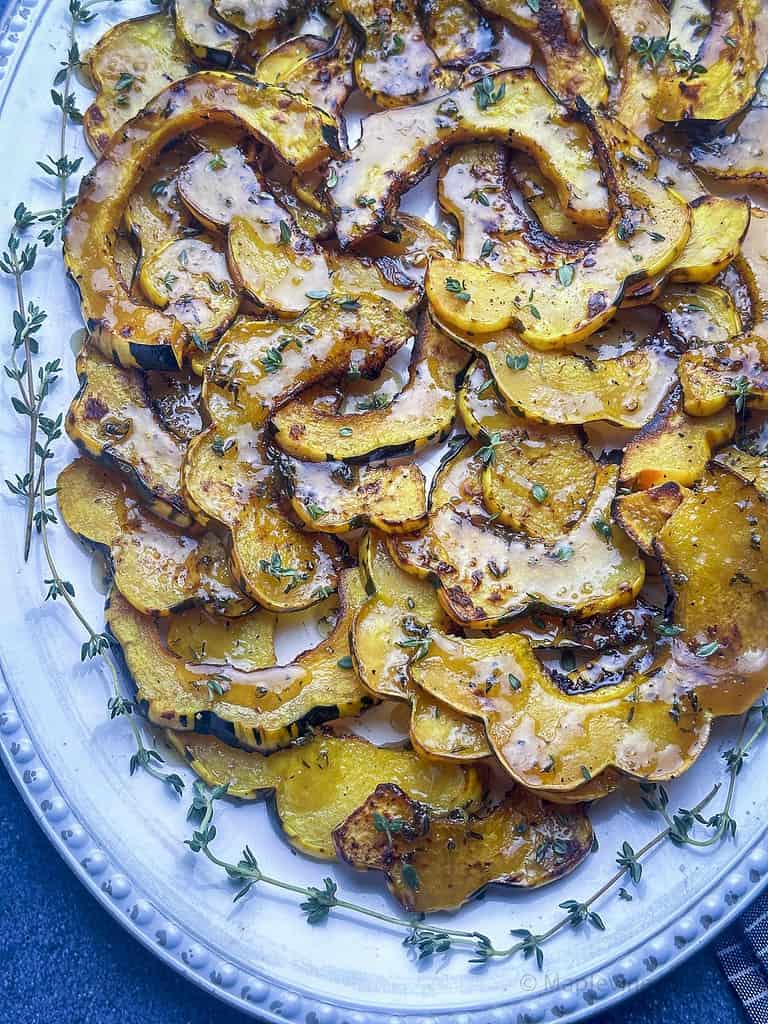 Roasted acorn squash slices on a platter with thyme sprigs.