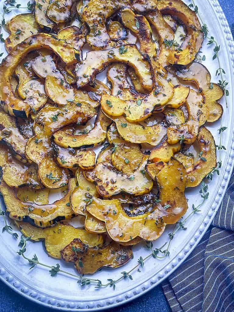 Roasted acorn squash slices on a platter with fresh thyme.