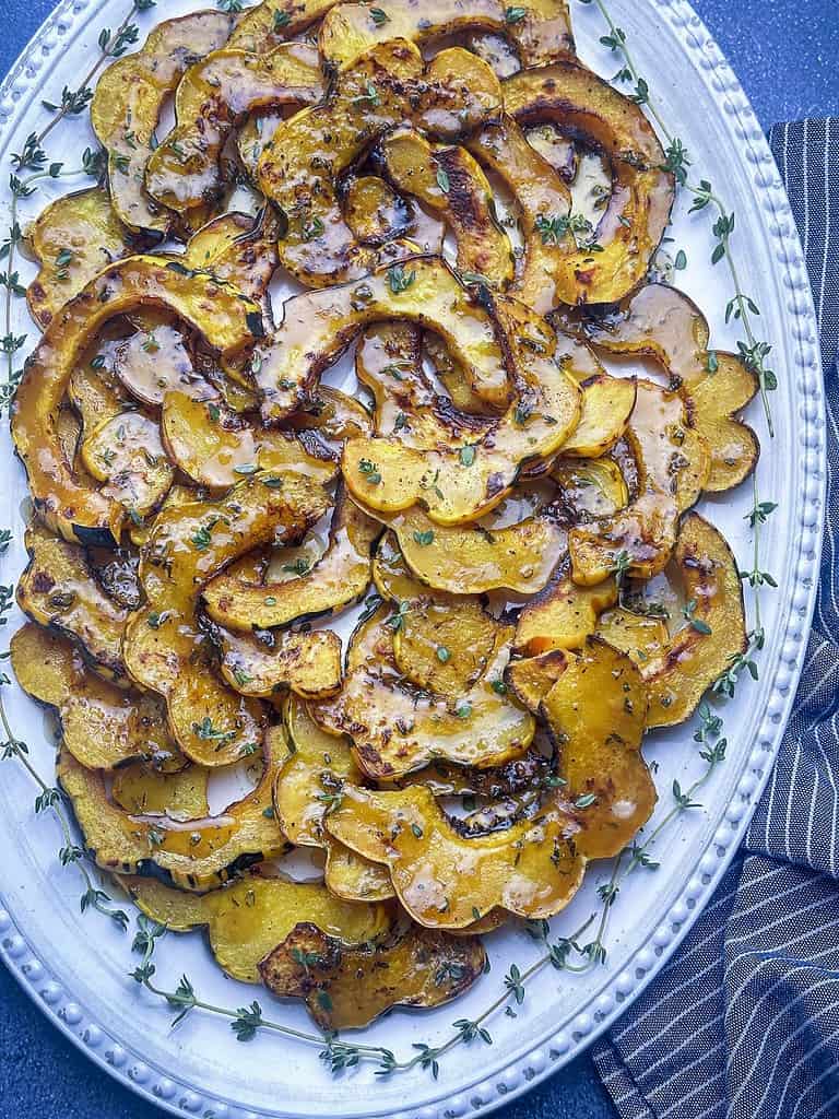 Roasted acorn squash slices on a platter with thyme sprigs.