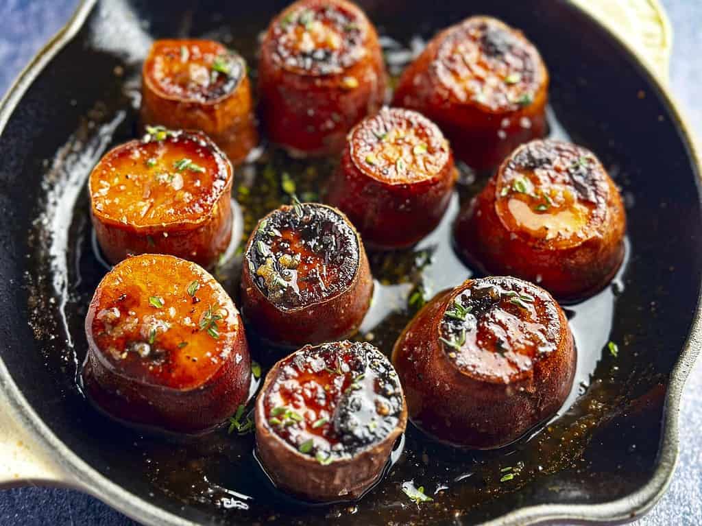Fondant sweet potatoes in a cast iron skillet with fresh thyme sprinkled on top.