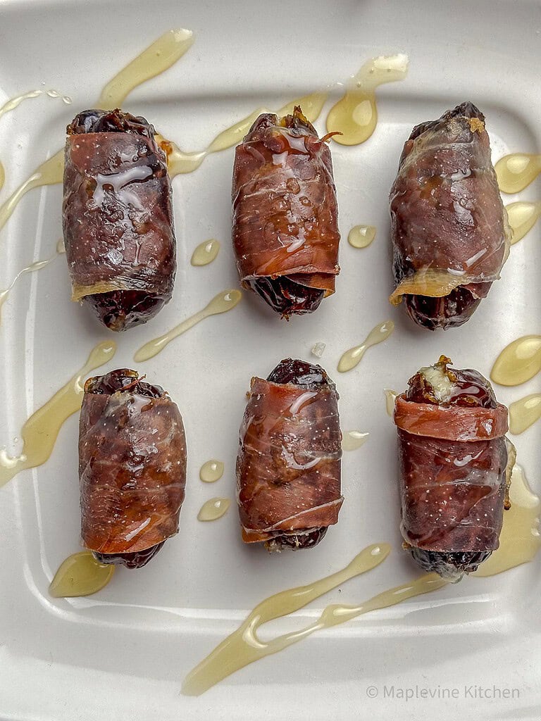 Prosciutto wrapped dates on a plate with a drizzle of honey.
