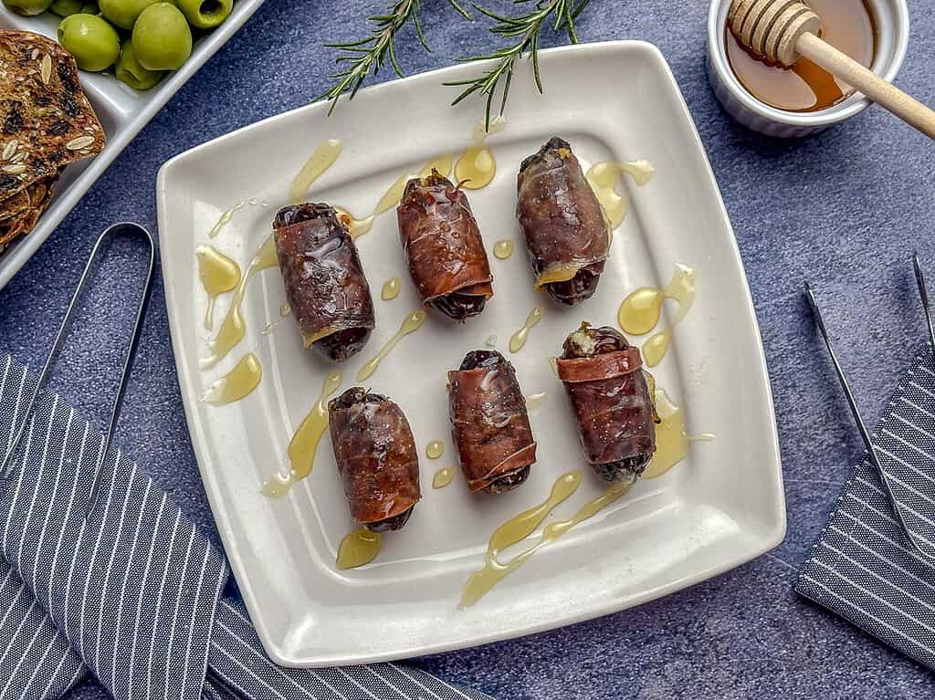 Prosciutto wrapped dates on a plate with a drizzle of honey.