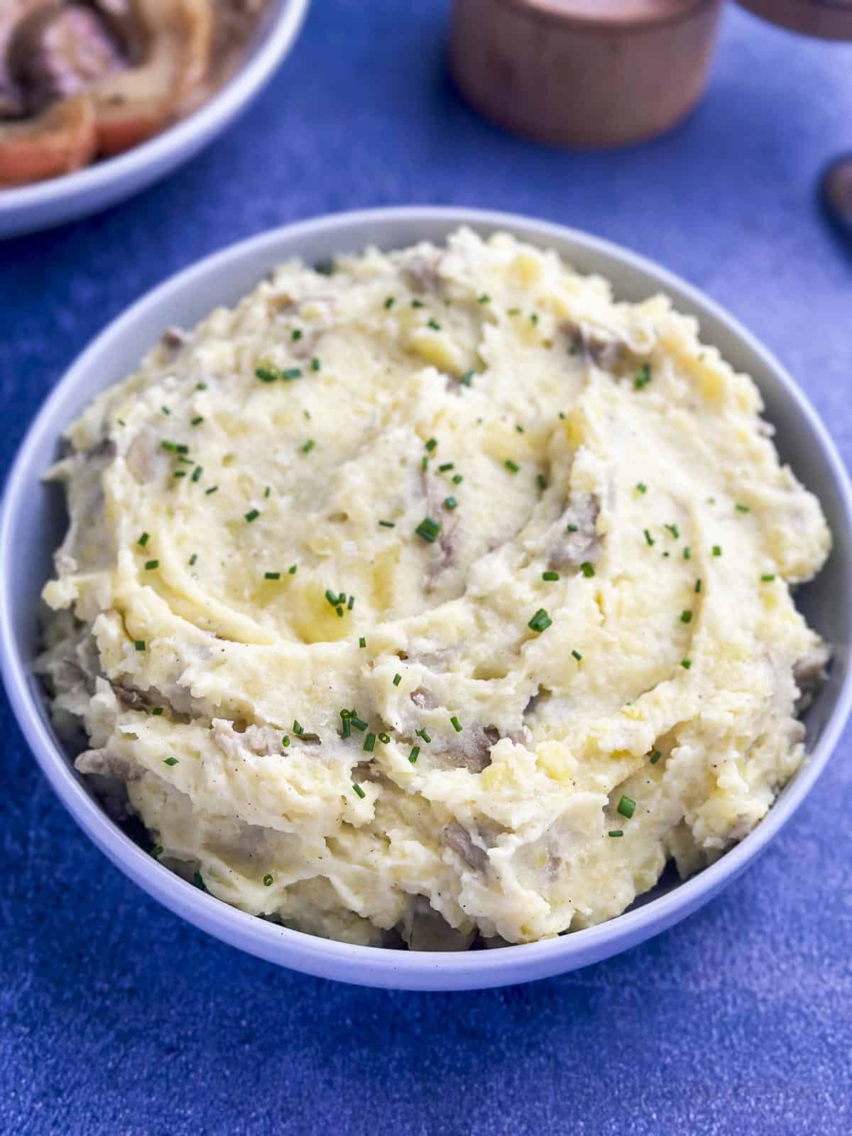 Yukon Gold mashed potatoes in a bowl with fresh chives for garnish.