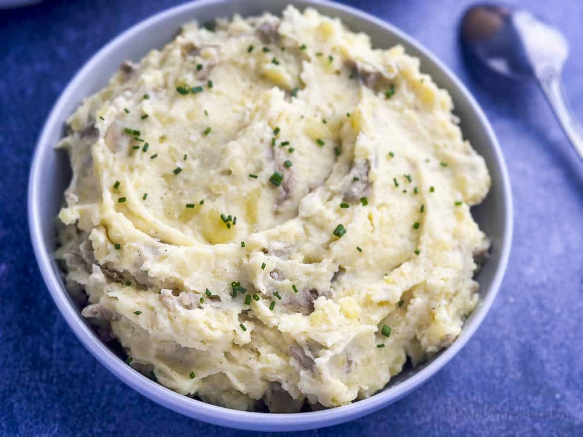 Mashed Yukon Gold potatoes with skins and chives on top in a bowl.
