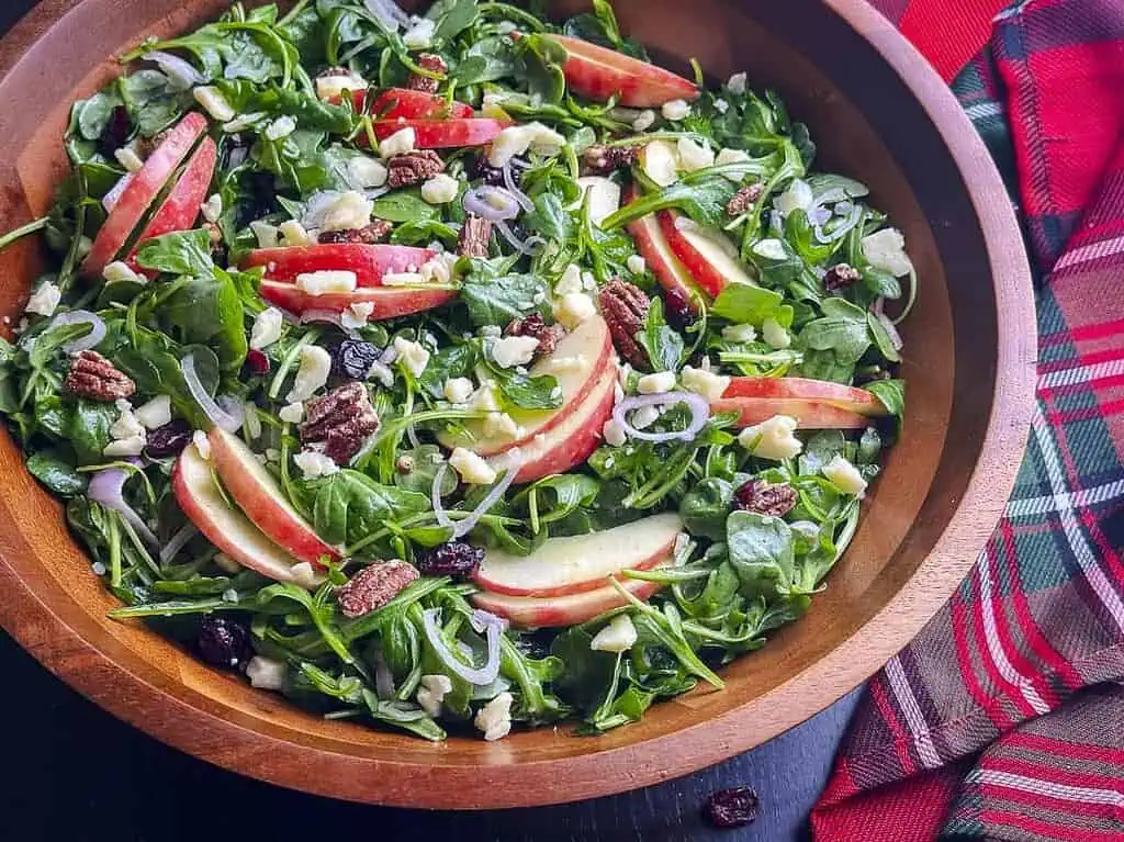 Arugula salad with apples, cheddar, pecans, and cranberries in a wooden bowl.