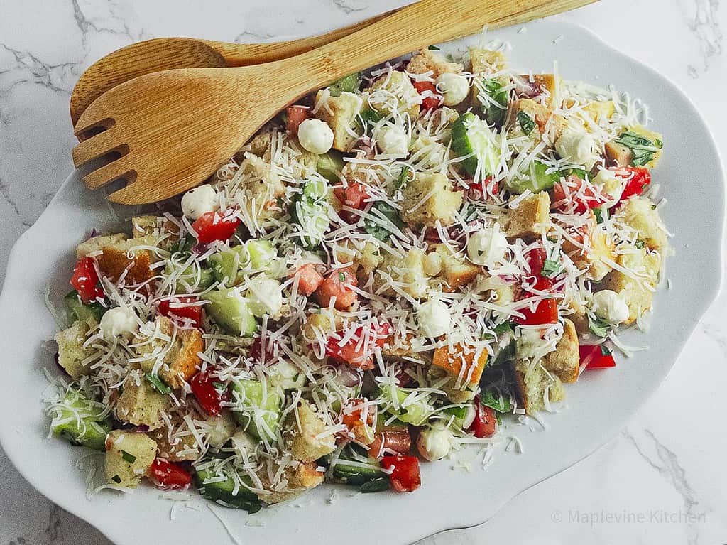 Panzanella salad on an oval white plate with wooden serving spoons.