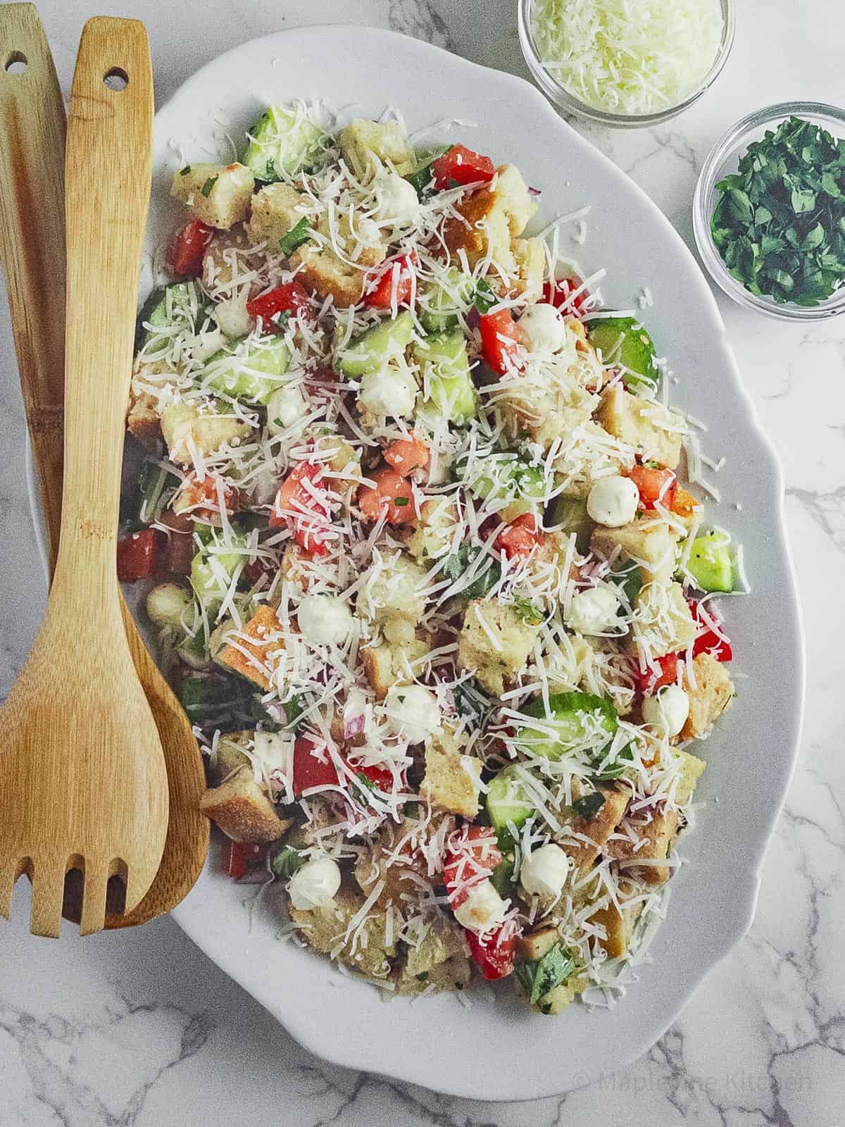 Panzanella salad on an oval white plate with wooden serving spoons.