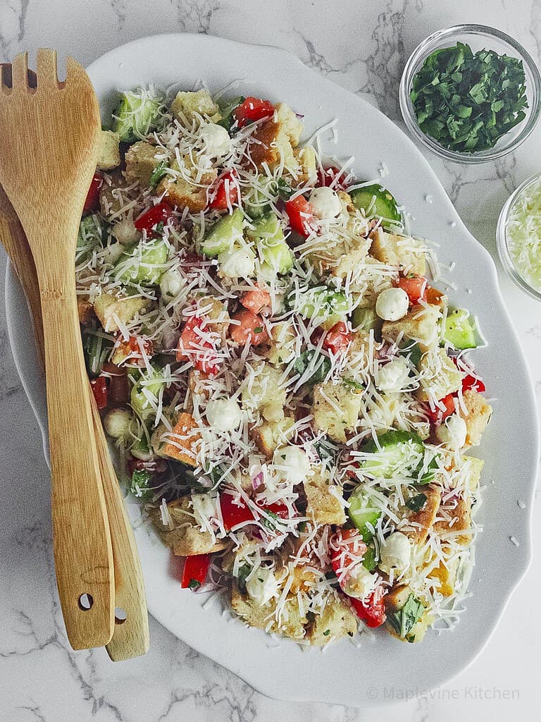 Panzanella salad on an oval white plate with wooden serving spoons.