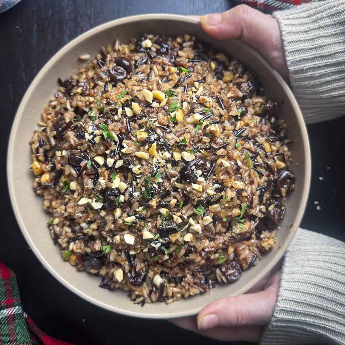 Wild rice with dried cherries and hazelnuts in a beige bowl with hands holding it