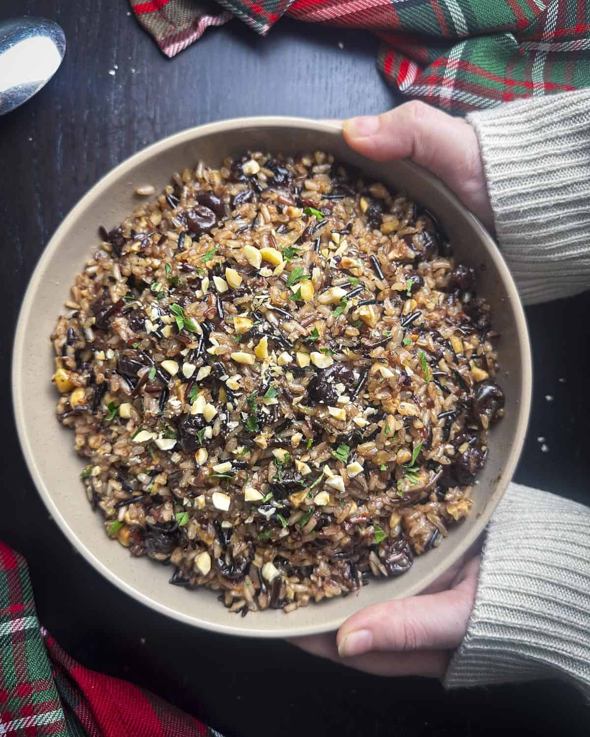 Wild rice with cherries and hazelnuts in a bowl held by two hands.