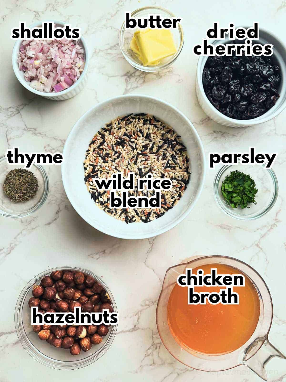 Ingredients for the wild rice with cherries and hazelnuts recipe laid out on a marble counter top and labeled.