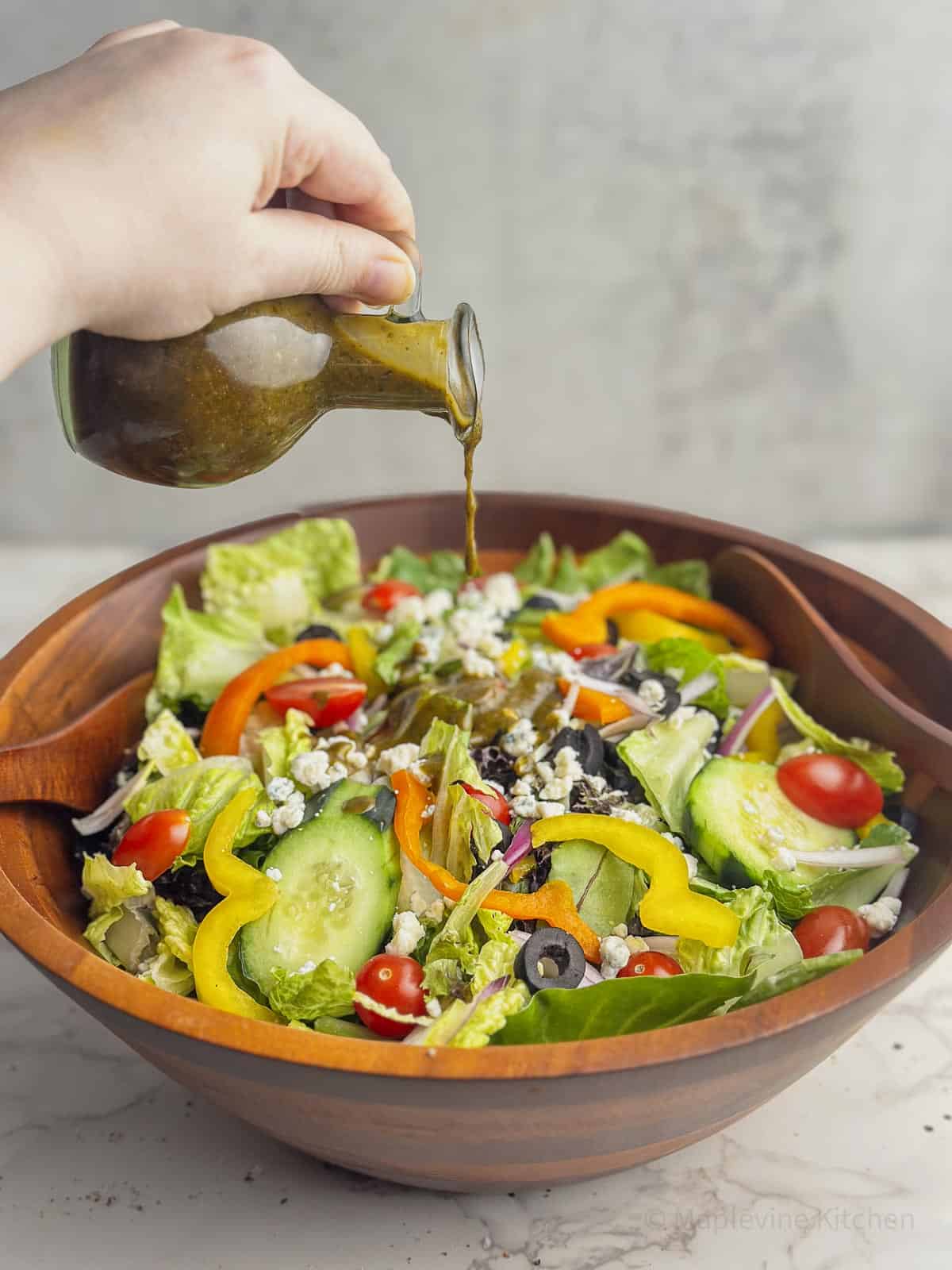 Balsamic basil vinaigrette in a carafe being poured over a salad in a wooden bowl.