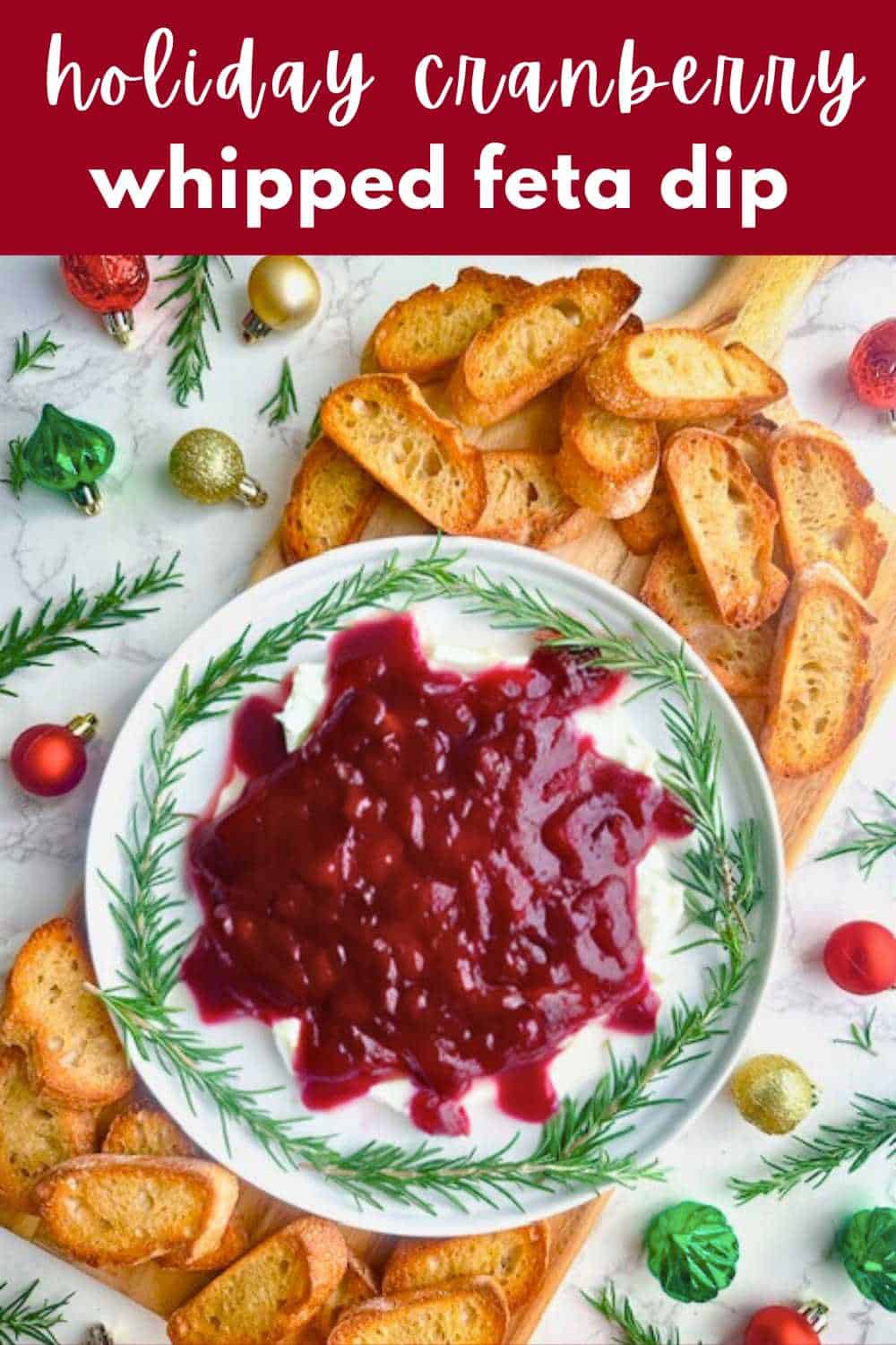 Cranberry whipped feta dip on a wooden board with crostini and fresh rosemary.