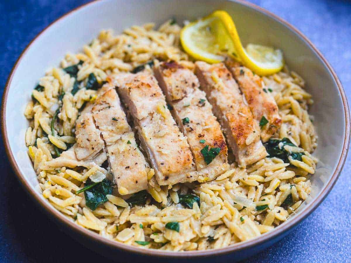 Creamy lemon orzo pasta topped with sliced chicken breast in a shallow bowl.
