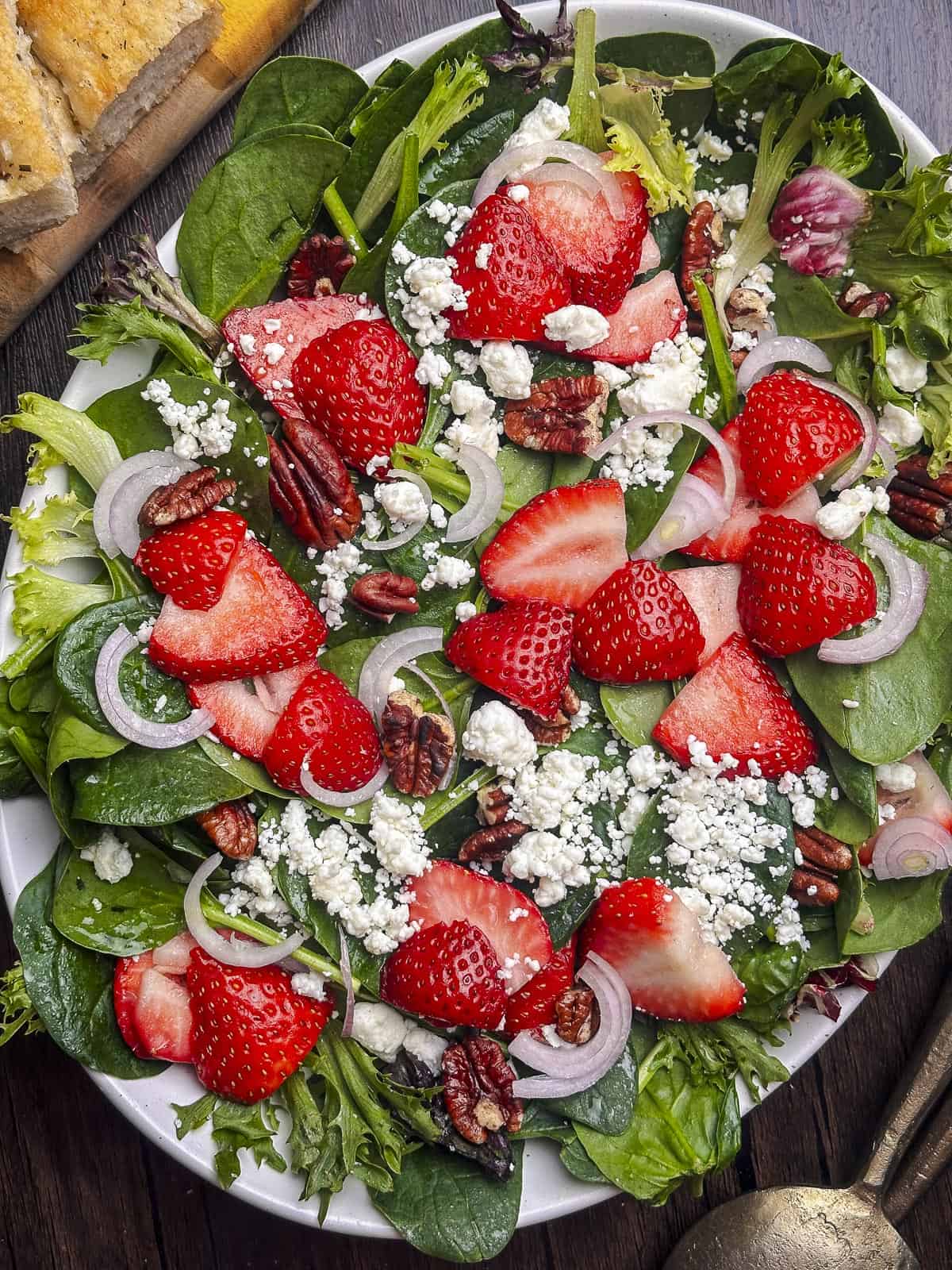 Mixed greens topped with sliced strawberries, goat cheese, and pecans on a white oval plate.