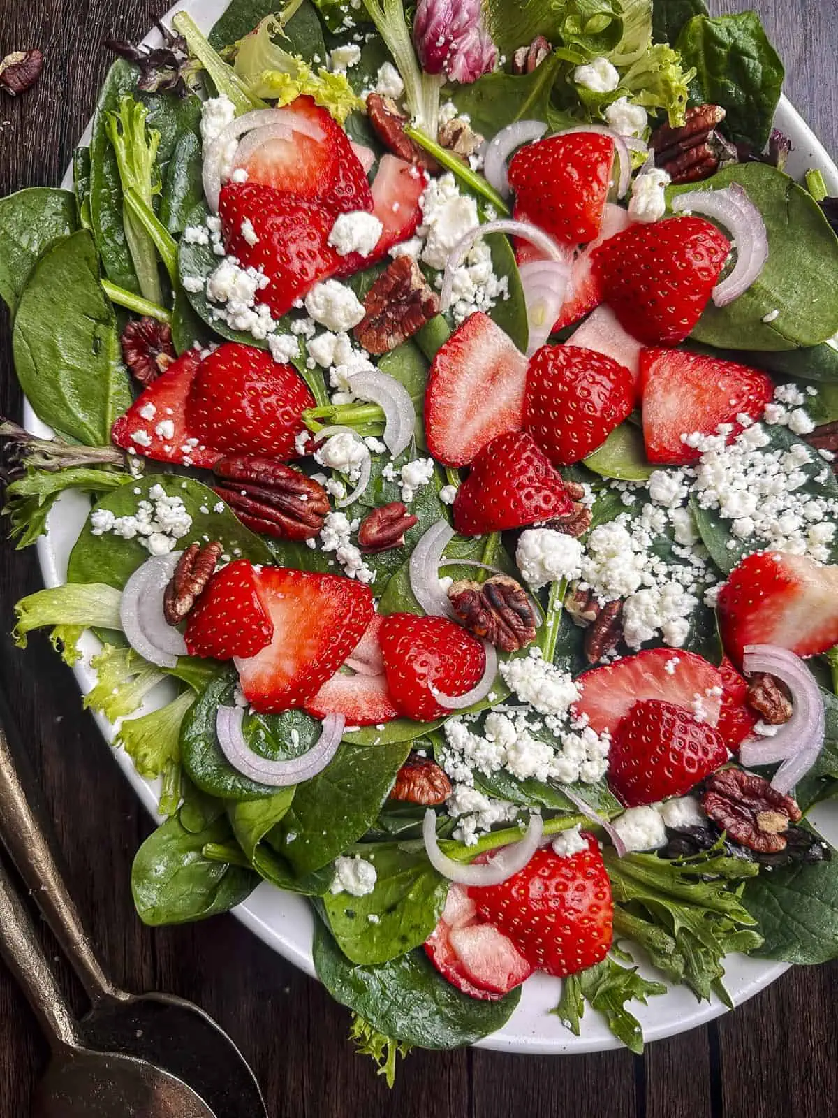 Strawberries, goat cheese, pecans, and mixed greens on a white oval plate.