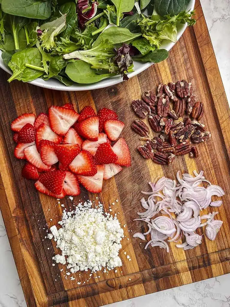 Ingredients for strawberry goat cheese salad on a wooden cutting board.