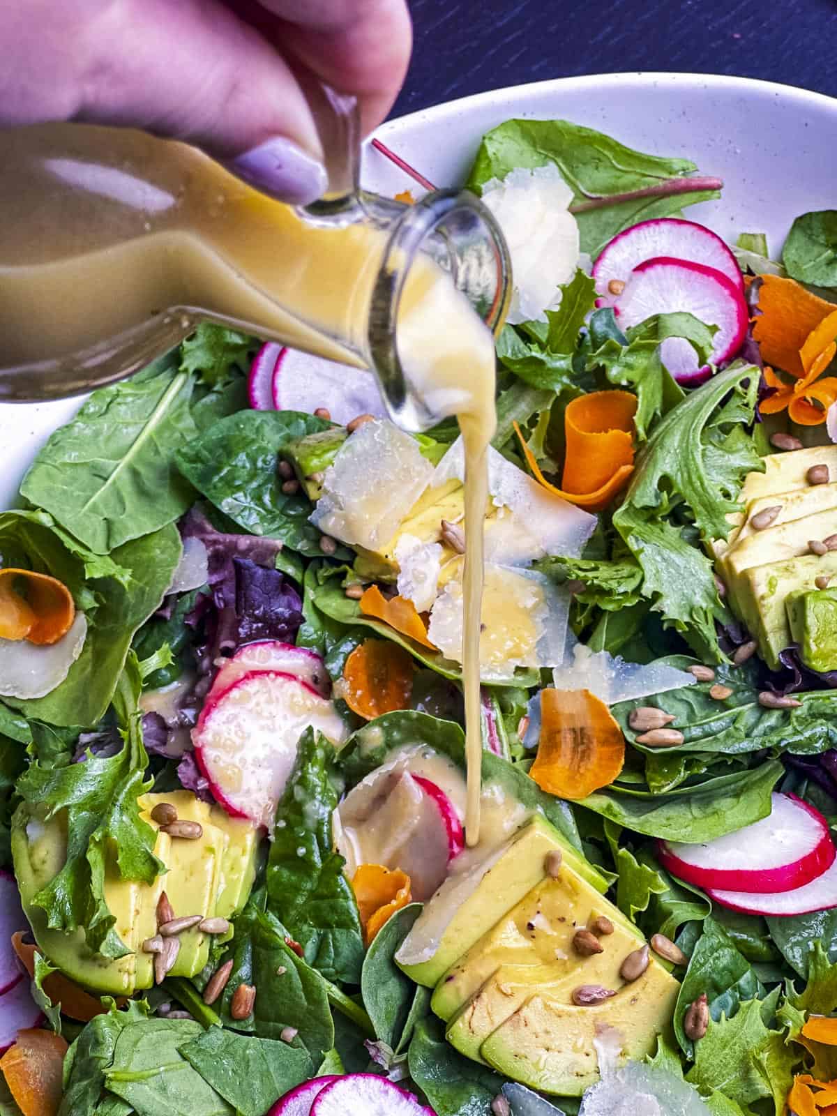 Lemon vinaigrette dressing pouring over a mixed greens salad.
