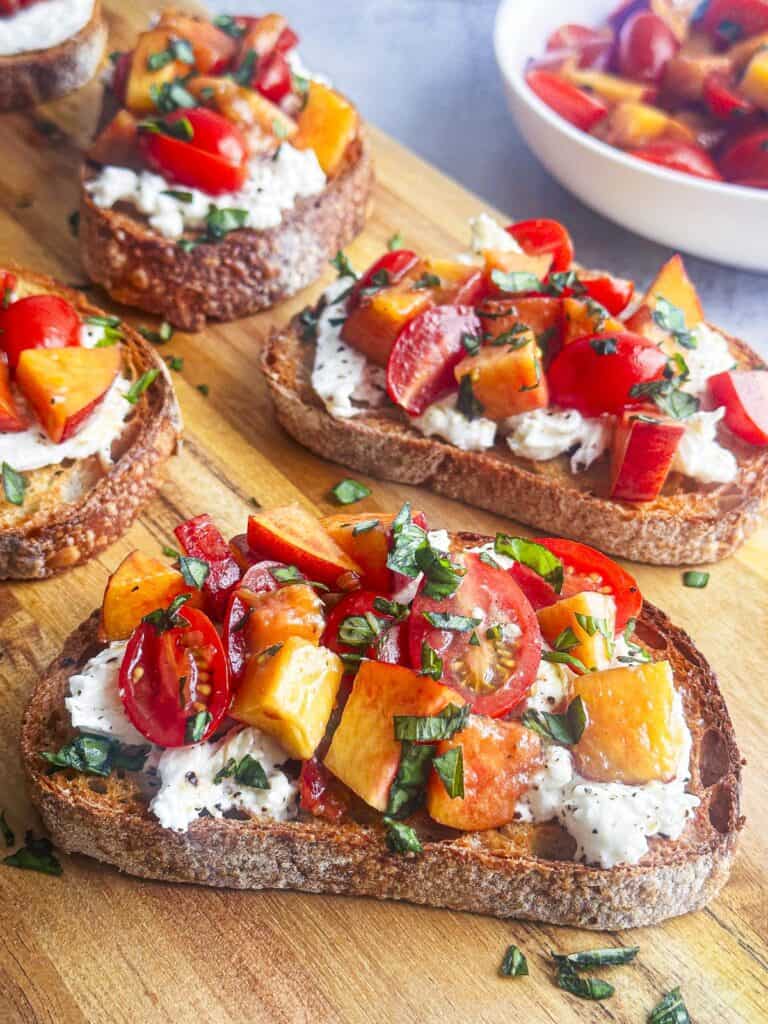 Fresh peaches, tomatoes, and burrata cheese on toasted bread slices.