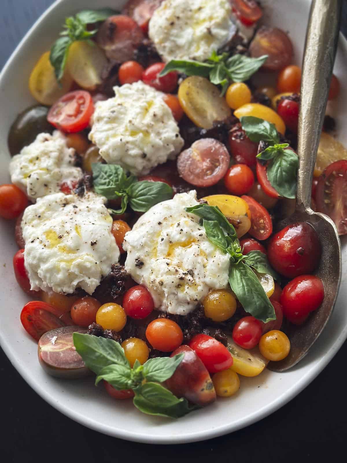 A plate of tomatoes, burrata cheese and basil.