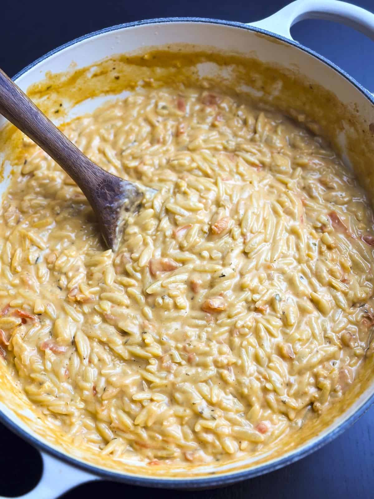Creamy tomato orzo pasta in a Dutch oven with a wooden spoon.