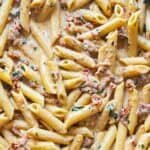 Close up of penne pasta in a creamy sauce with sun-dried tomatoes and basil.