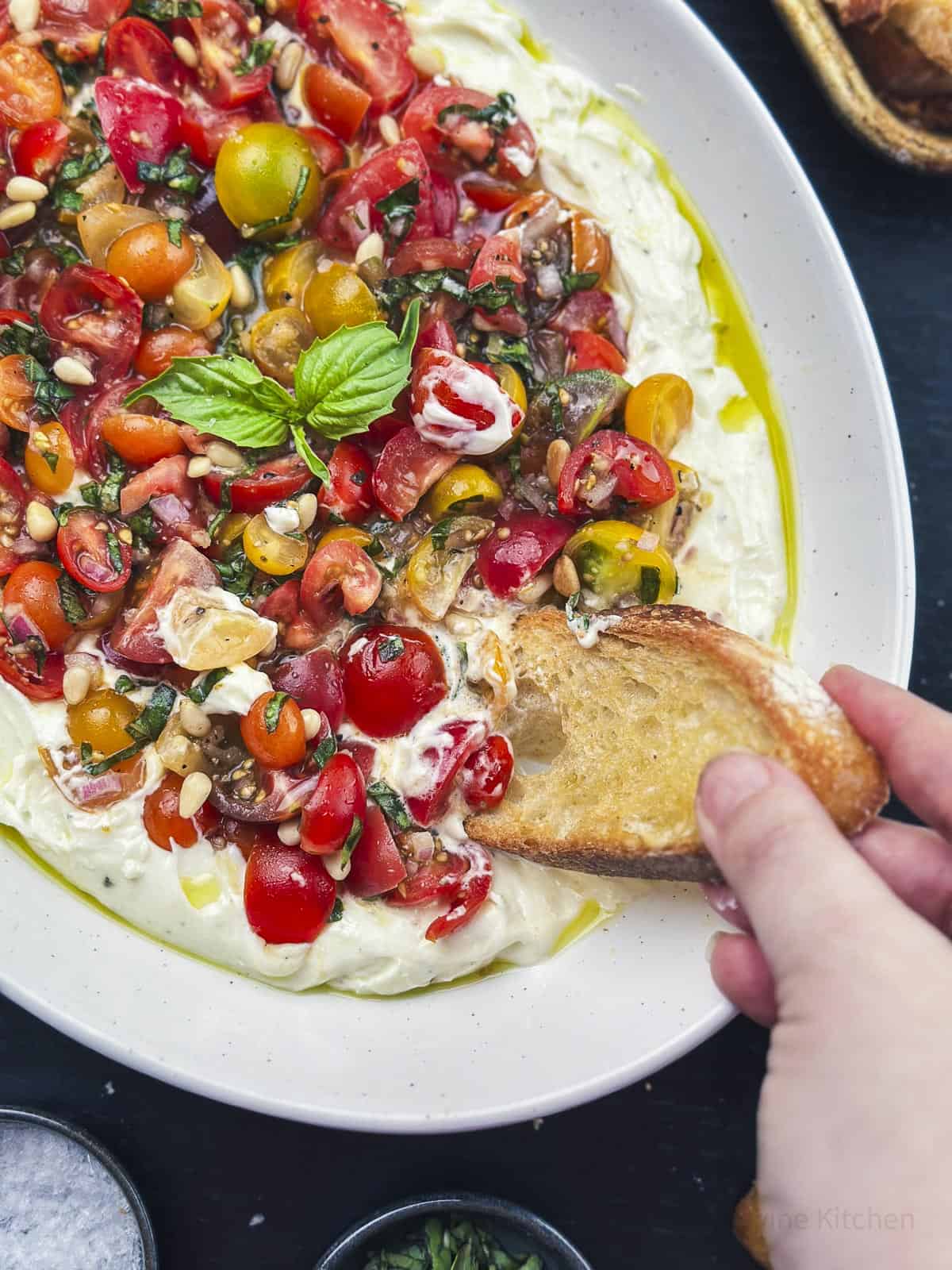 Bruschetta dip with a hand dipping bread.