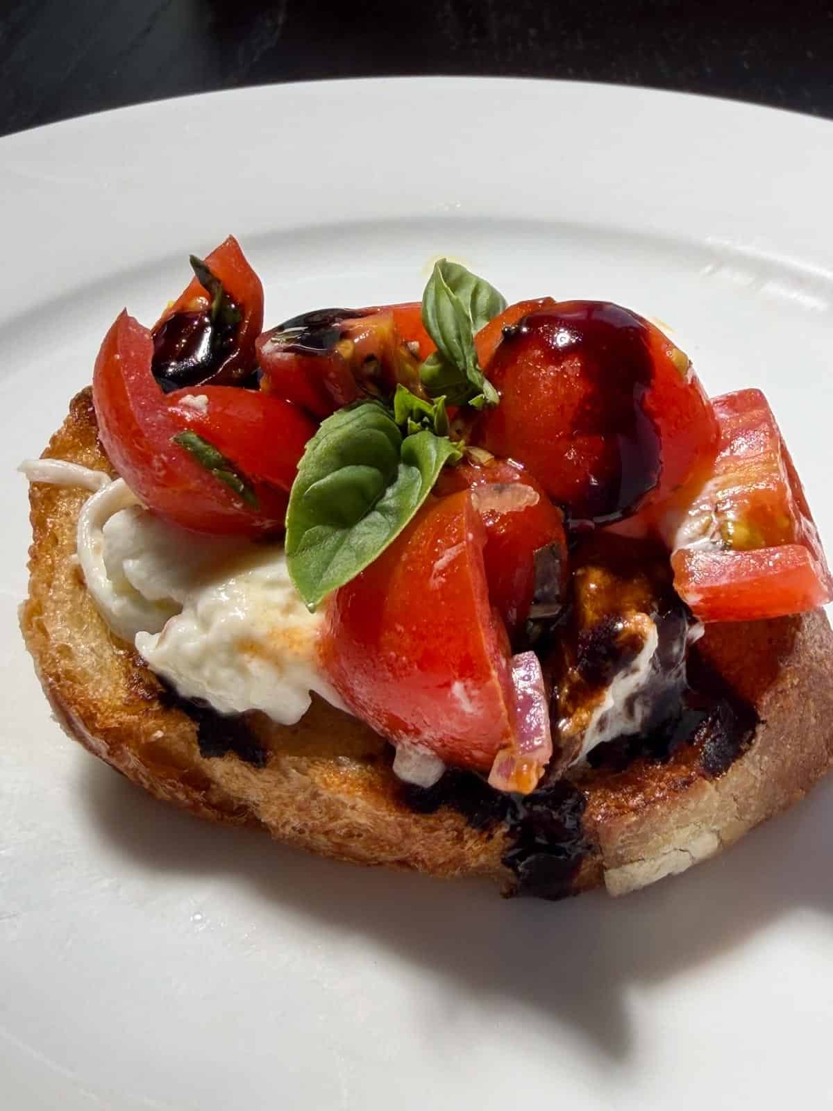 A crostini topped with burrata cheese, tomato bruschetta, and drizzled with balsamic.