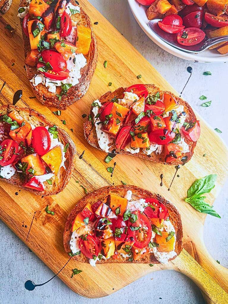 Burrata bruschetta on toasted bread with peaches, tomatoes, and fresh basil leaves.