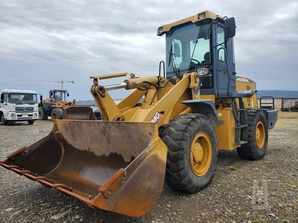 Maquinaria pesada: cargadora frontal amarilla en un sitio de construcción o parqueo, con otras máquinas en el fondo, ideal para optimizar operaciones de obra civil y levantamiento de materiales.