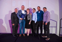 Group of seven professionals on stage at a corporate event.