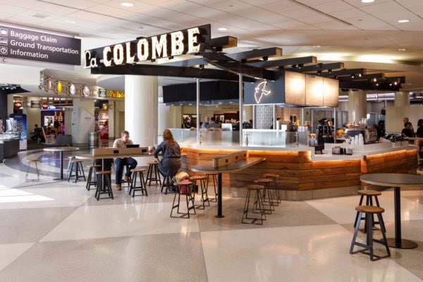 La Colombe coffee shop at an airport terminal with seating and travelers.