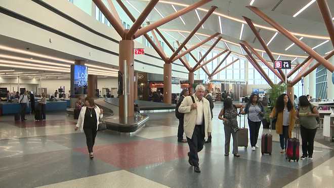 Passengers walking through an airport terminal with wooden beams and large windows.