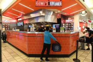 Geno's Steaks counter inside a shopping mall with customers and staff.