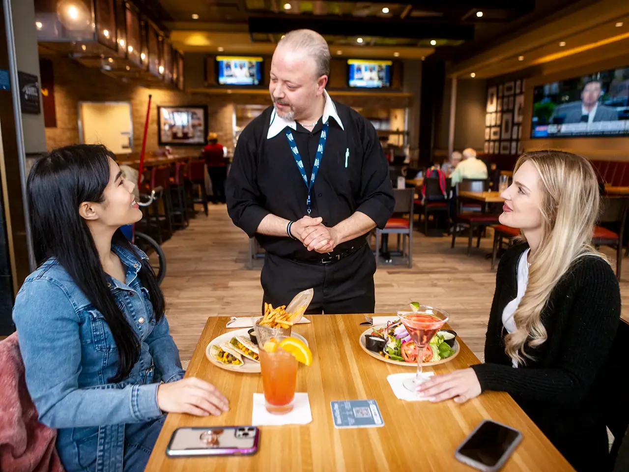 Waiter receiving feedback on food from customers seated at table in restaurant at airport (Customer Service)