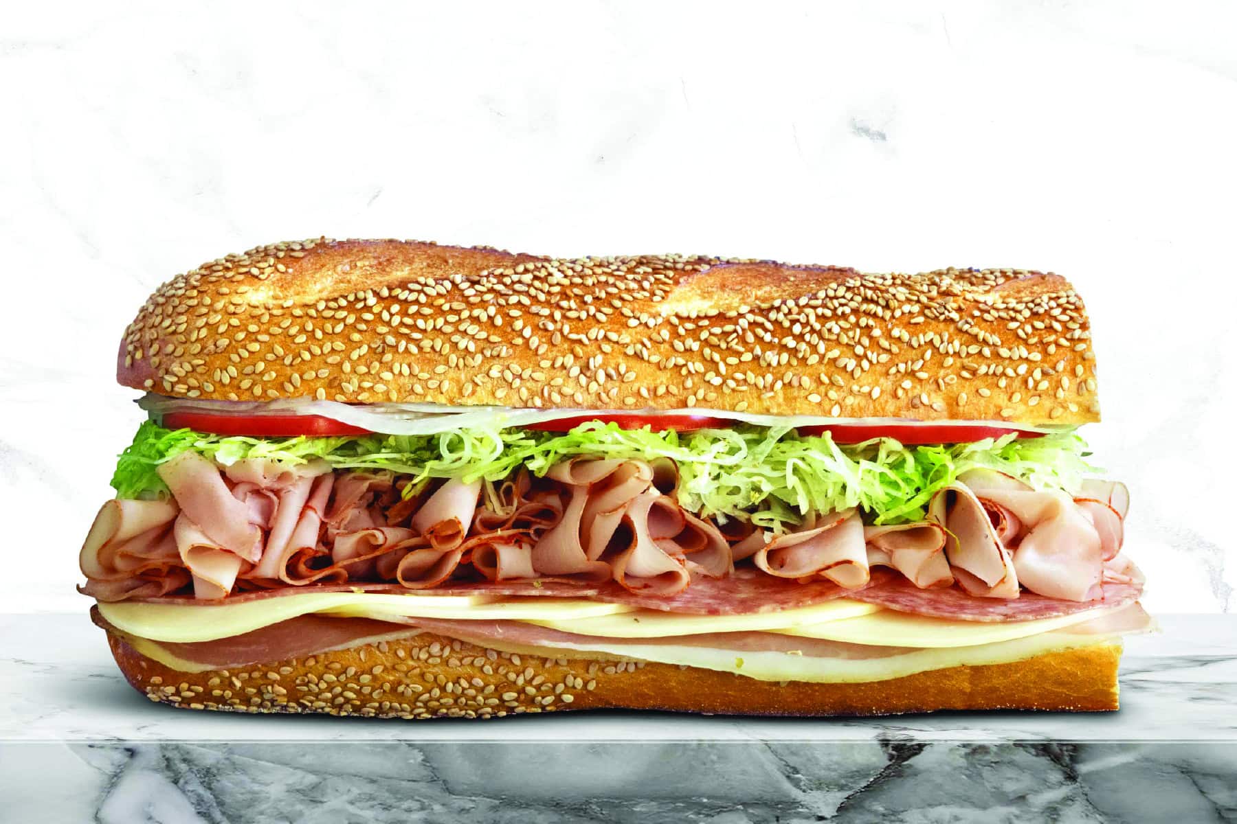 Sub sandwich with ham, turkey, lettuce, tomato, and cheese on a sesame seed bun.