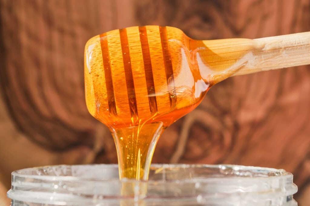 Honey flows from a wooden stick for honey into a jar
