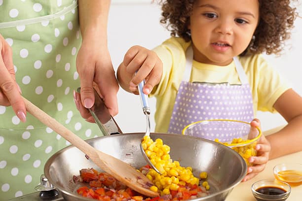 Freshly prepared healthy meals being cooked by a caregiver and a child emphasizing nutritious food for children served by Meals in Motion