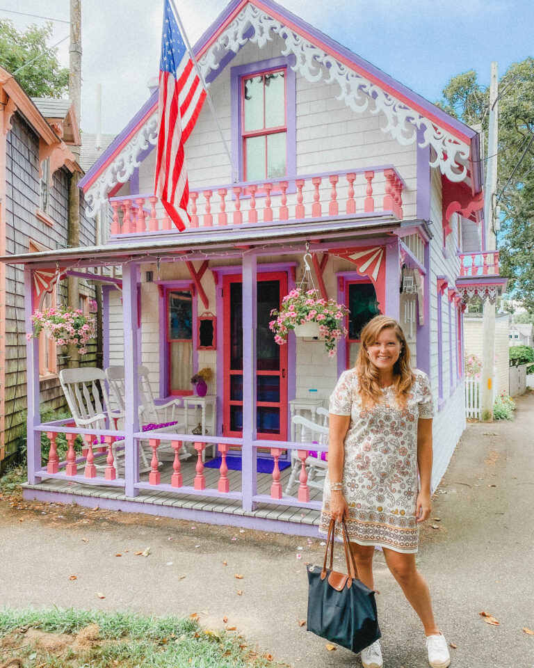 These are the traditional Gingerbread Houses of Martha's Vineyard. This one looks like a small Barbie dream house, as it's only maybe one and a half stories, and painted in purple and pink trim. It also has ornate wood carvings around the corners of the home, and a few rocking chairs on the small porch.