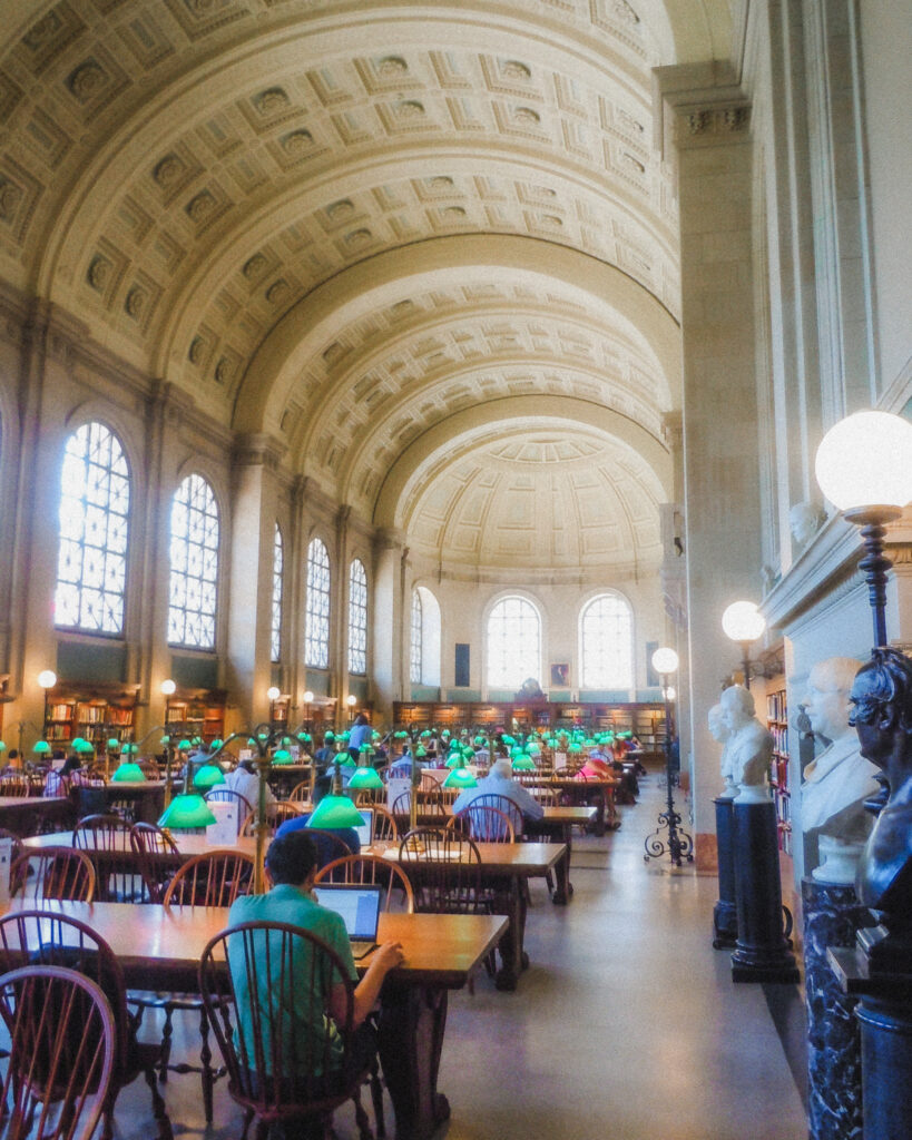 This is one of the most well known rooms in the Boston Public Library in Boston, Massachusetts. It is a large hall with tall ceilings that have almost floor to ceiling curved windows, and rows of tables adorned with vintage green lamps.