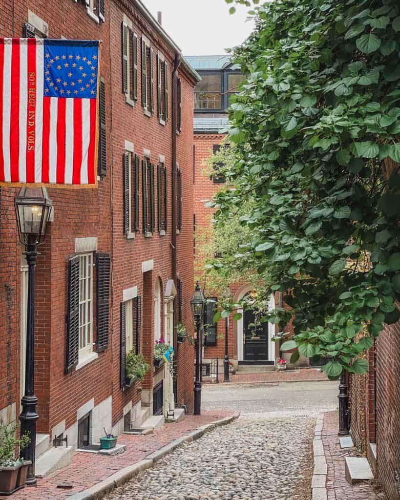This street is one of the most famous in Boston and the USA. It's located in Beacon Hill which is one of the best places to stay in Boston your first time. It's surrounded by brownstones but the street is actually made with cobblestone. The brownstones that line the street have patriotic American flags hanging, and window boxes bursting with flowers. You can also spot a historic oil lamp at the bottom of the street.