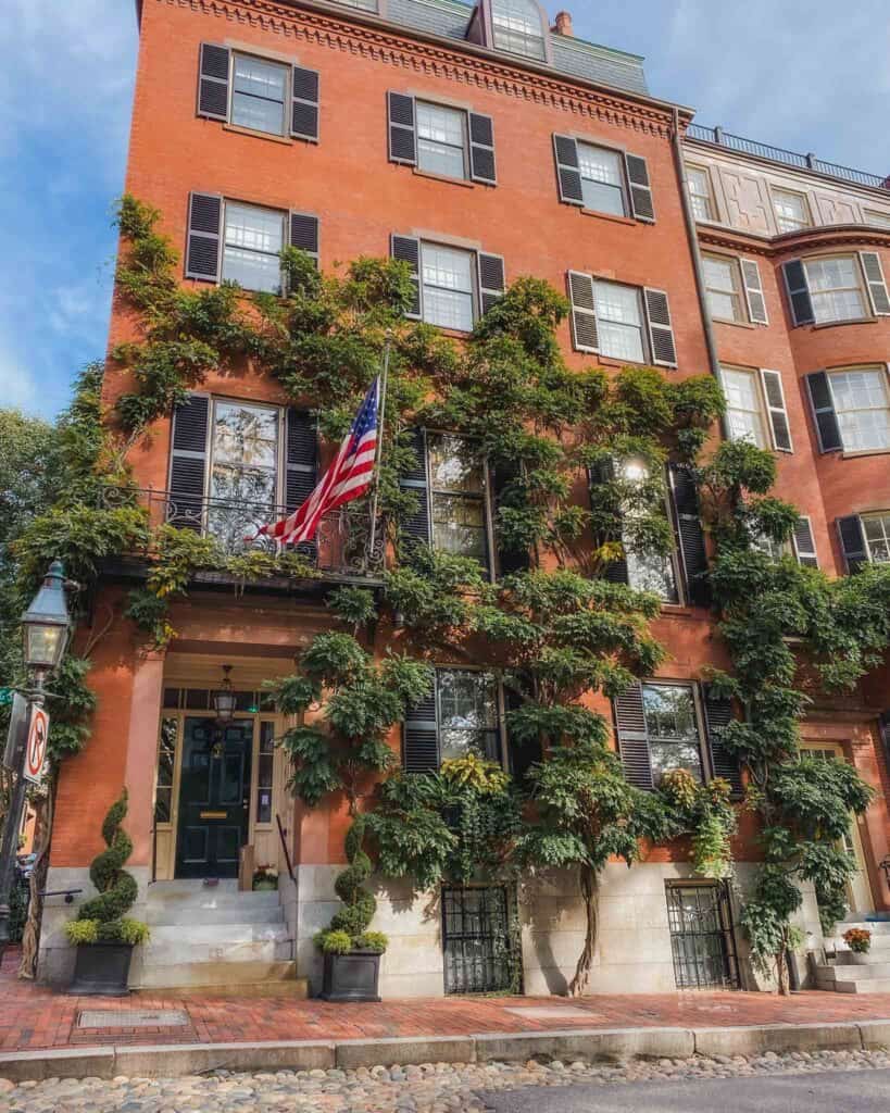 This beautiful brownstone is in the heart of Beacon Hill in Louisburg Square. This specific brownstones has wisteria cascading down the front and the window boxes are adorned with flowers. It also has an American flag flying proudly on the front, and a historical oil lamp in front since it's right on the corner. This square is surrounded with brownstones and a garden in the middle. 